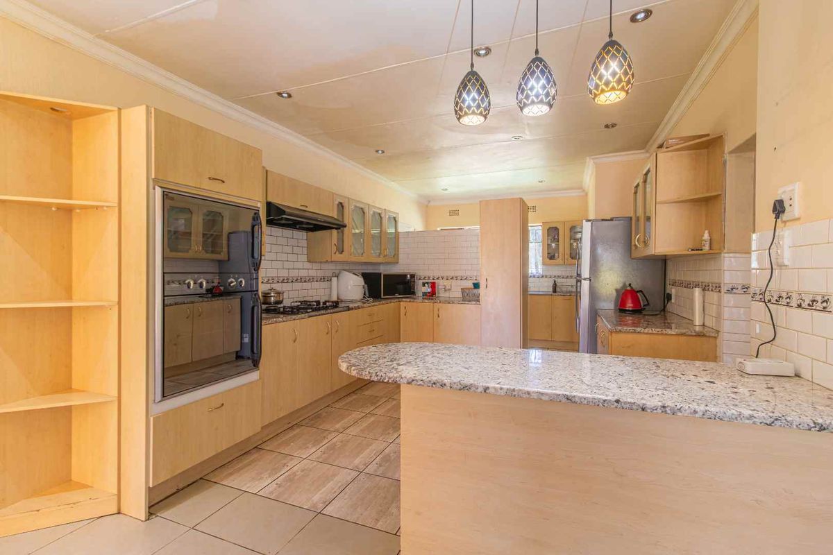 Spacious kitchen featuring granite countertops, subway tile backsplash, built-in oven, gas hob, and ample cabinetry with pendant lighting.