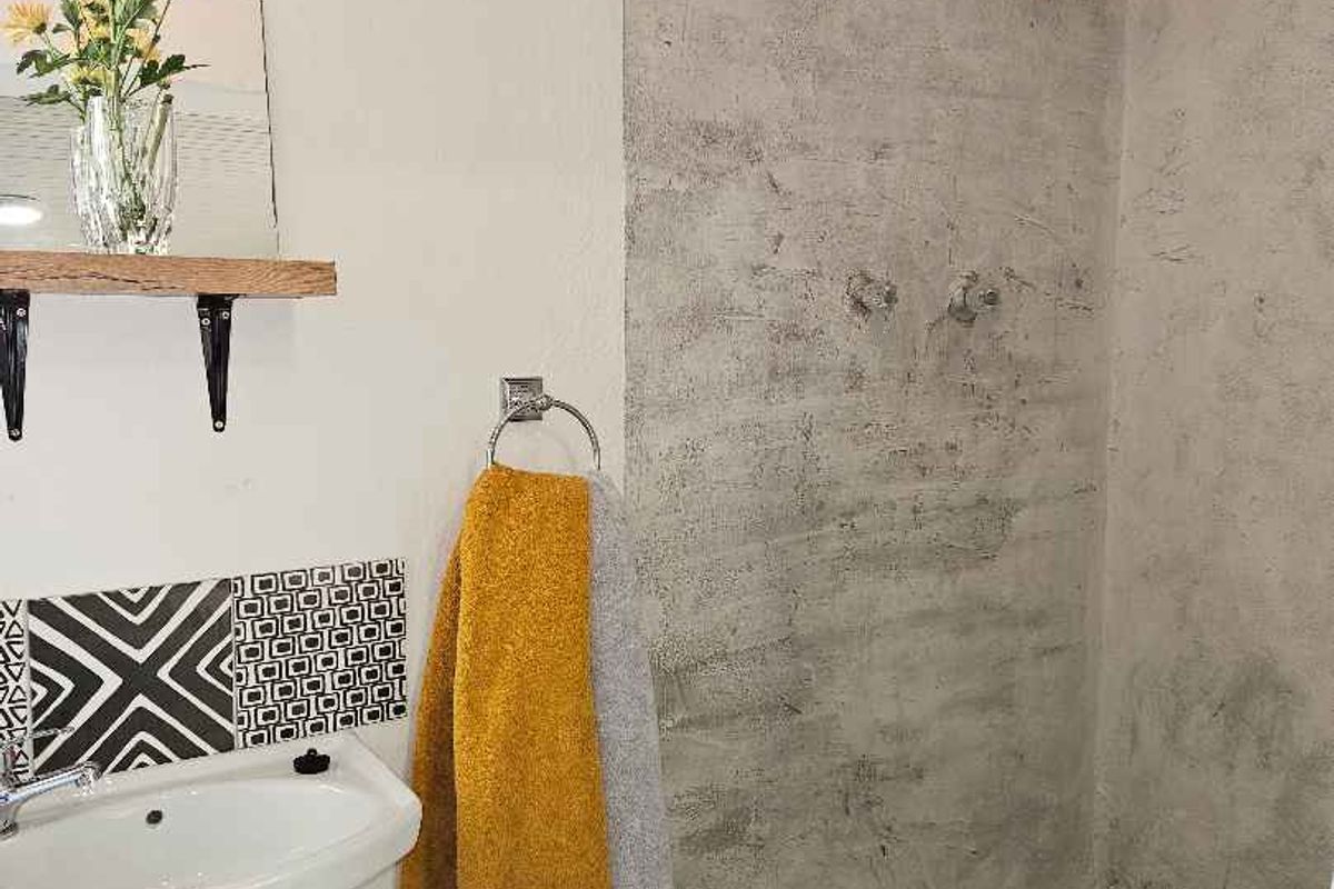 A compact bathroom featuring a walk-in shower with a stone-tiled floor, a wall-mounted basin, and decorative patterned splashback tiling.
