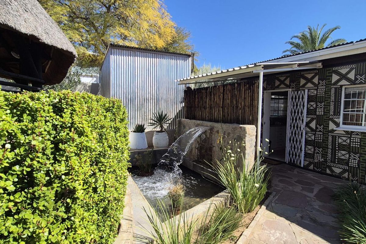 Rear exterior area featuring a stone water feature, paved walkway, and access to the main dwelling with decorative exterior wall finishes.