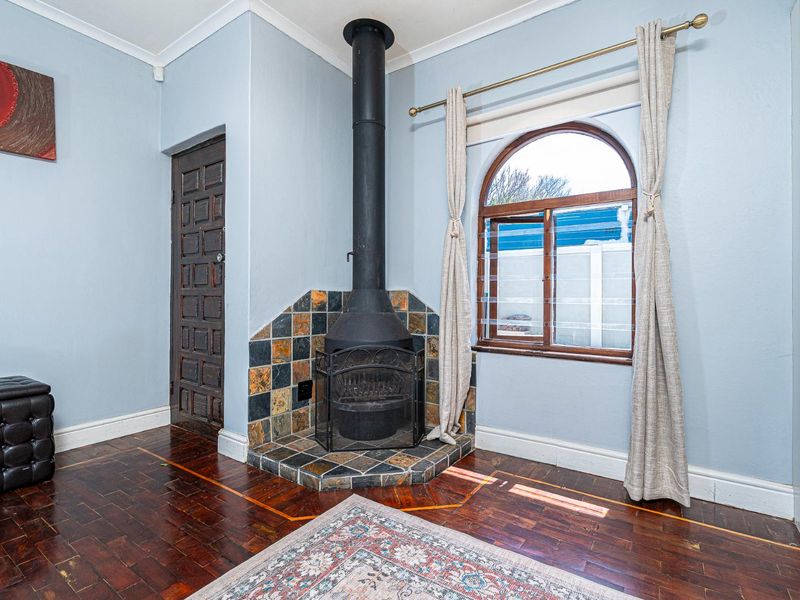 Living room featuring a corner freestanding fireplace with a slate hearth, classic parquet flooring, and an arched window.