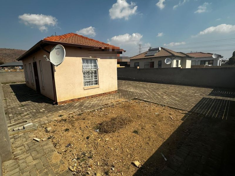 Rear view of the property featuring a tiled roof, paved driveway, and a large unlandscaped garden area enclosed by a boundary wall.