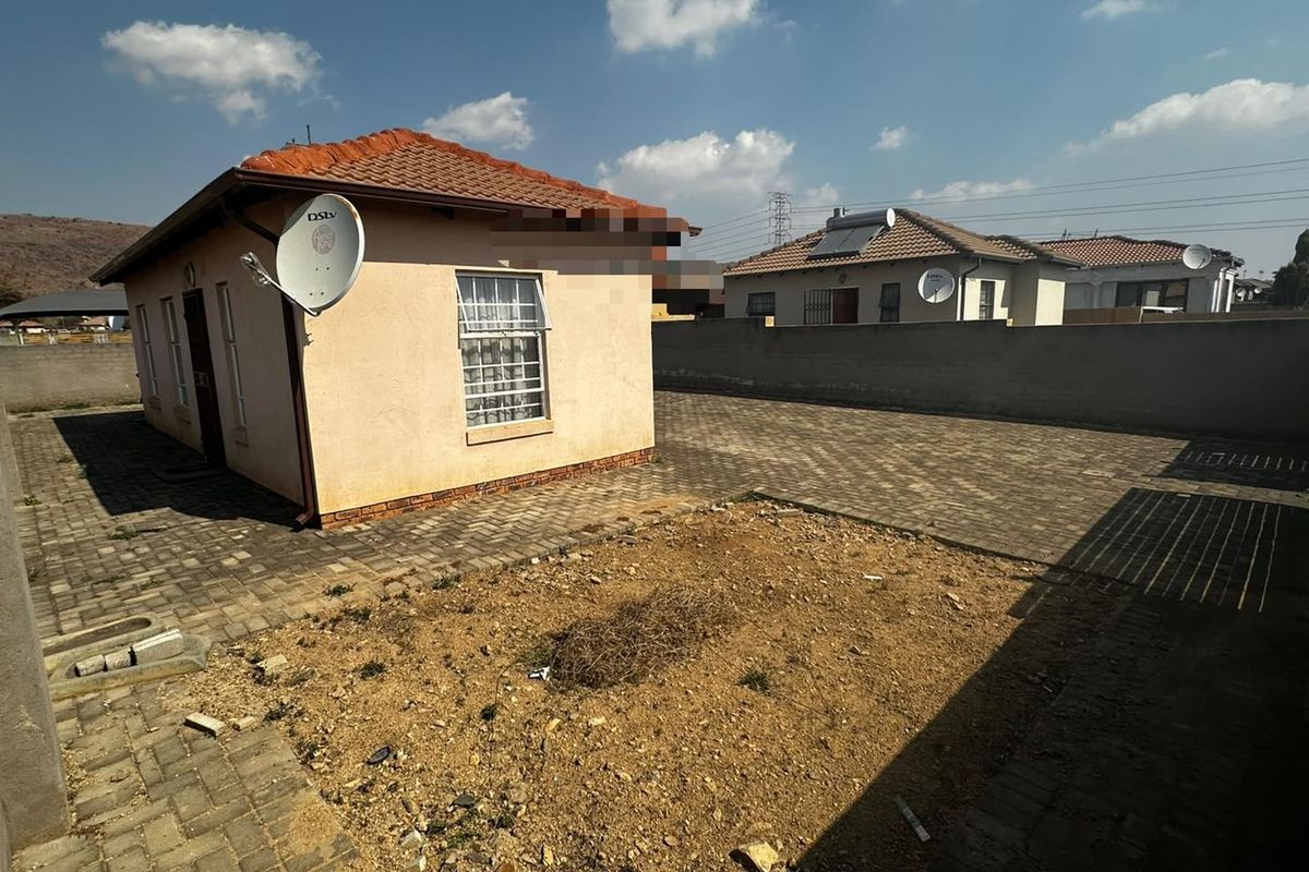 Rear view of the property featuring a tiled roof, paved driveway, and a large unlandscaped garden area enclosed by a boundary wall.