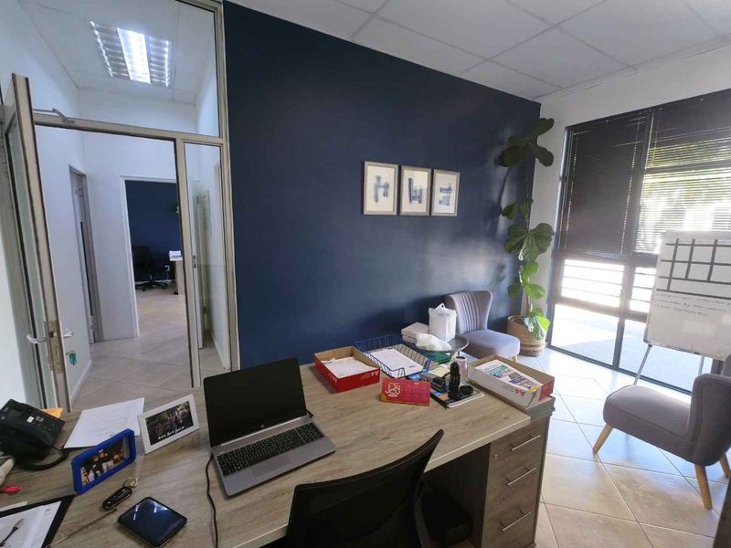 A functional office space featuring a dark accent wall, tiled flooring, and a glass partition providing a view into the adjacent workspace.