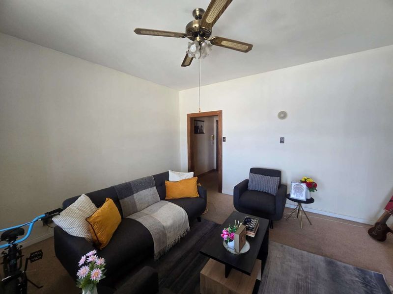 A living room featuring a ceiling fan and neutral wall finishes, providing a functional space with access to an adjoining hallway.