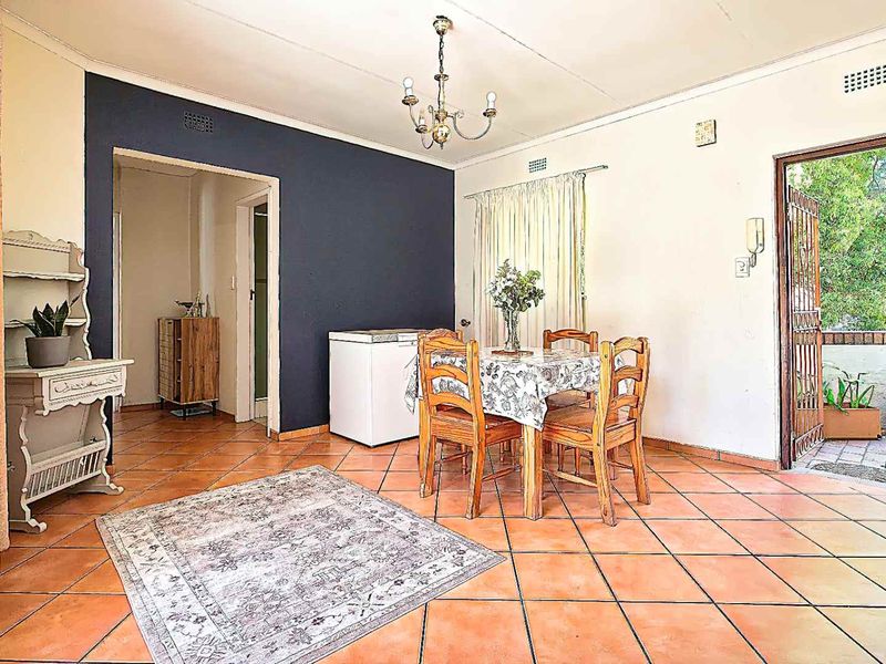 Dining area featuring terracotta tiled flooring, a central chandelier, and direct access to an outdoor patio through a security gate.
