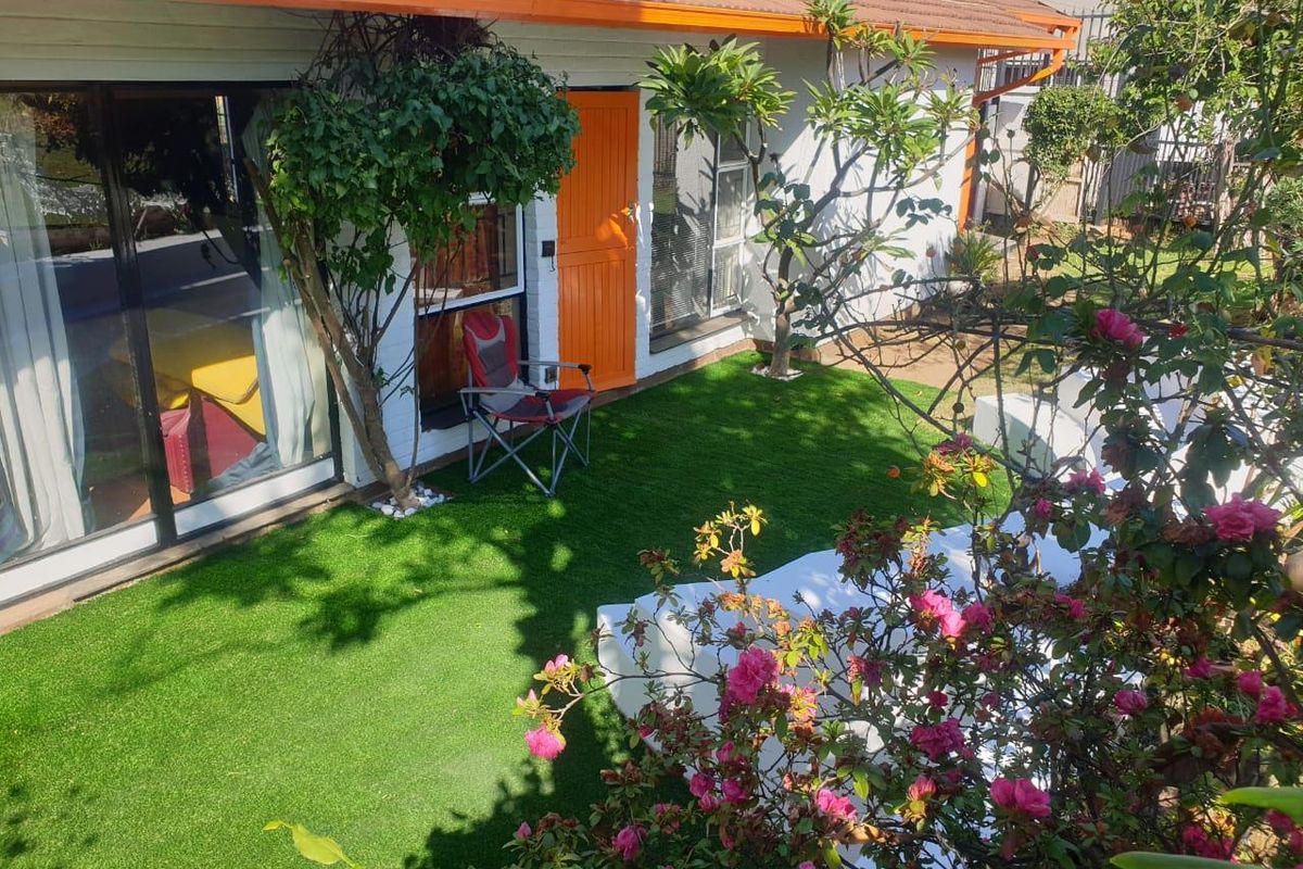 A well-maintained rear garden area featuring artificial turf, built-in seating, and direct access to the home via sliding glass doors.