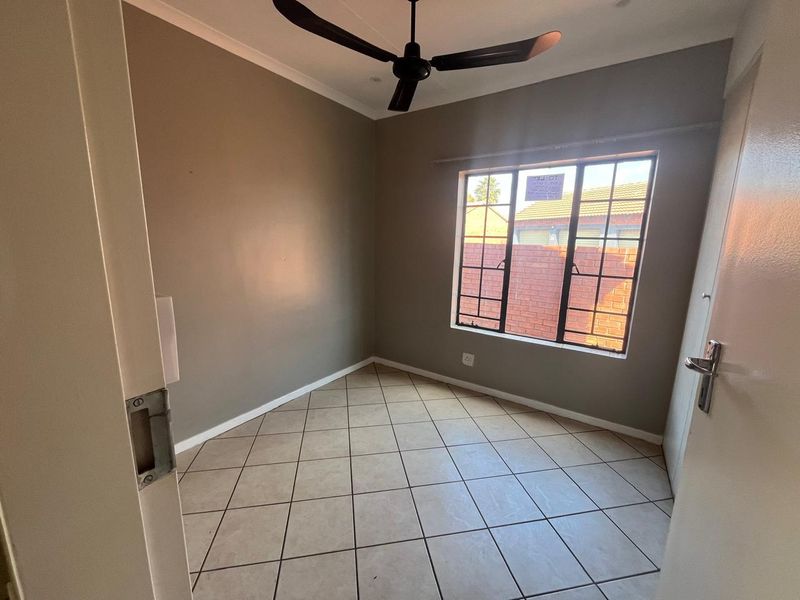 A clean, empty bedroom featuring neutral wall paint, tiled flooring, and a ceiling fan, offering a versatile space ready for personalization.