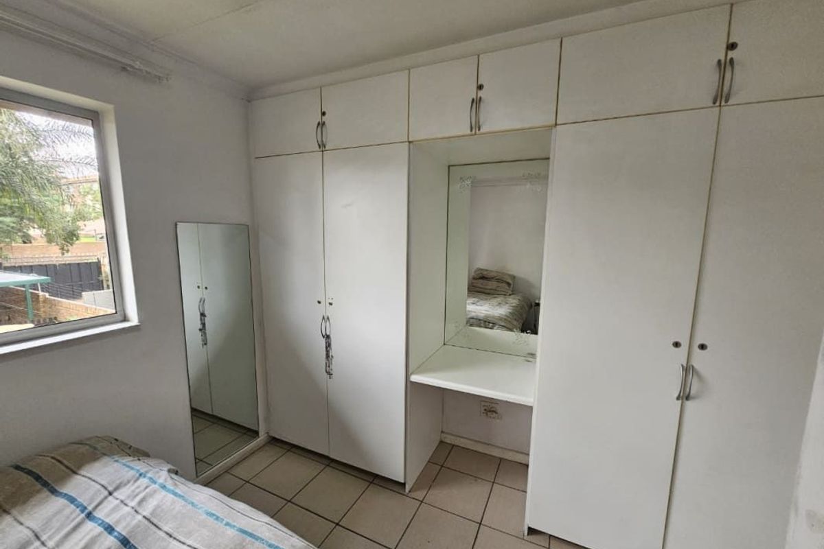 A bedroom featuring built-in white cupboards with an integrated vanity area and tiled flooring.