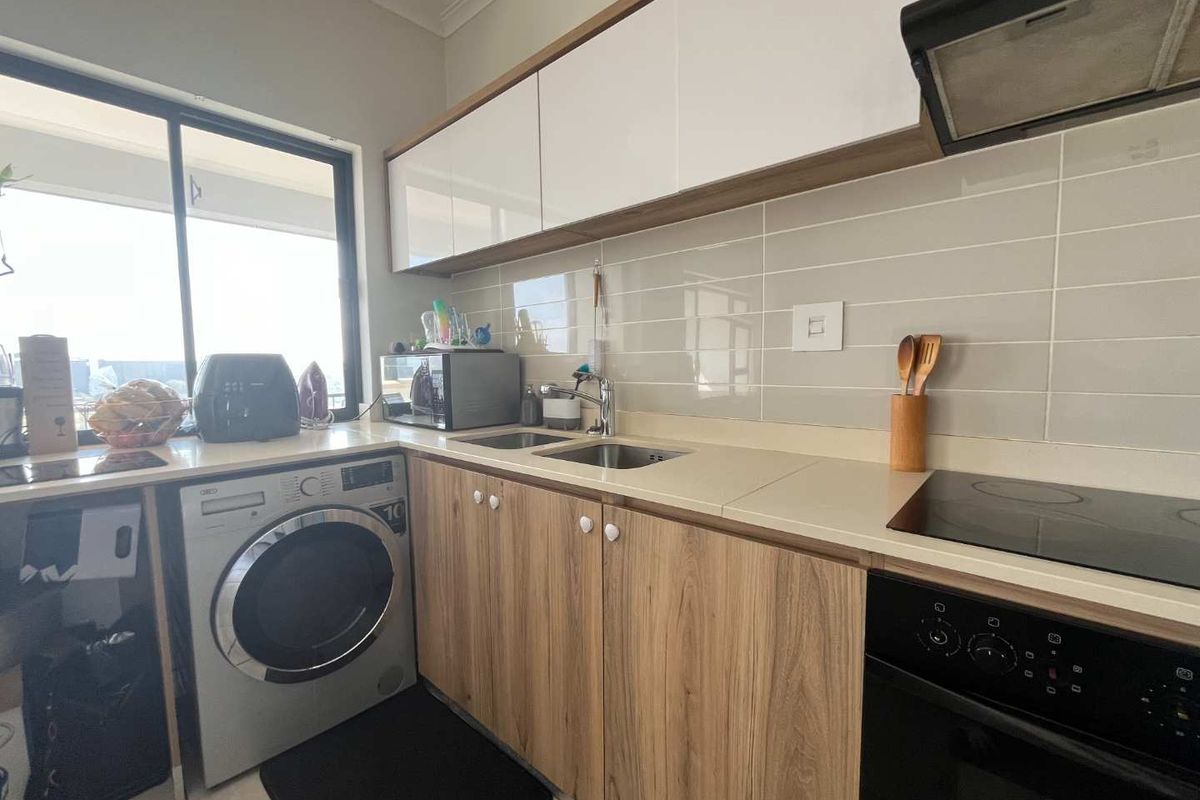 Modern kitchen featuring wood-grain cabinetry, stone-look countertops, integrated electric hob and oven, extractor fan, and a built-in laundry appliance connection.