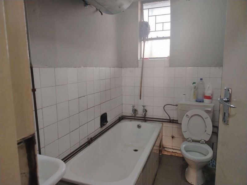 A dated bathroom featuring a standard bathtub, toilet, and basin with exposed plumbing and tiled wall finishes, requiring modernization and cosmetic updates.