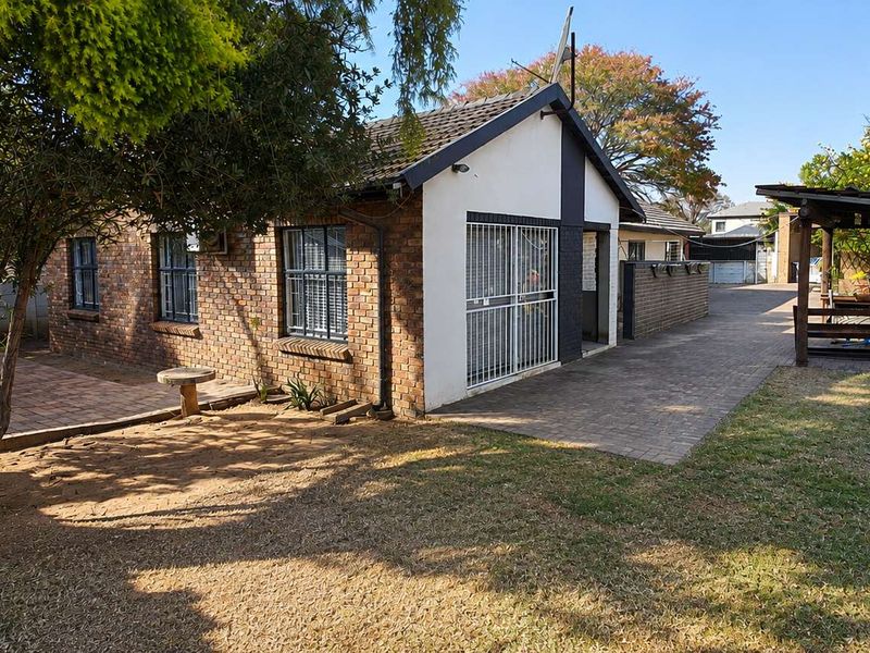 Rear view of the property featuring a brick facade, paved patio area, and a timber pergola structure set within a private garden.