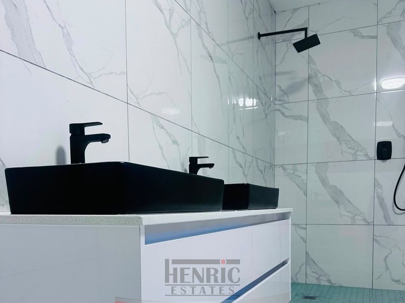 Modern bathroom featuring a double vanity with black vessel sinks, matte black fixtures, and elegant marble-look wall tiling.