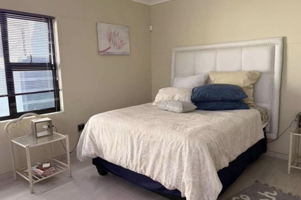A functional bedroom featuring tiled flooring, neutral wall finishes, and an aluminium-framed window.