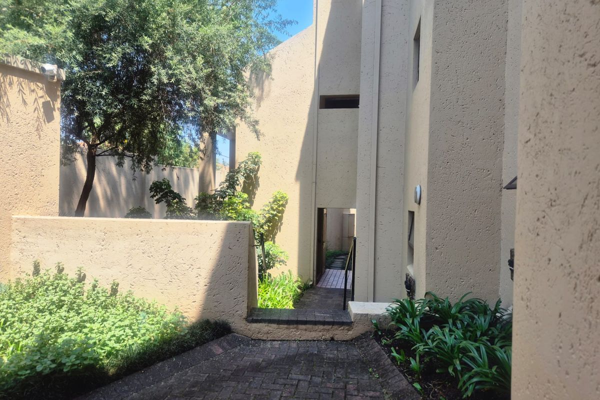 A view of the rear exterior area featuring a paved walkway, textured walls, and established garden landscaping.