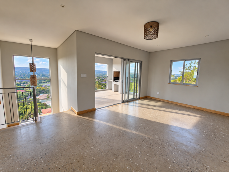 Spacious, light-filled living area featuring polished concrete floors, large windows with scenic views, and seamless access to a covered patio with a built-in braai.
