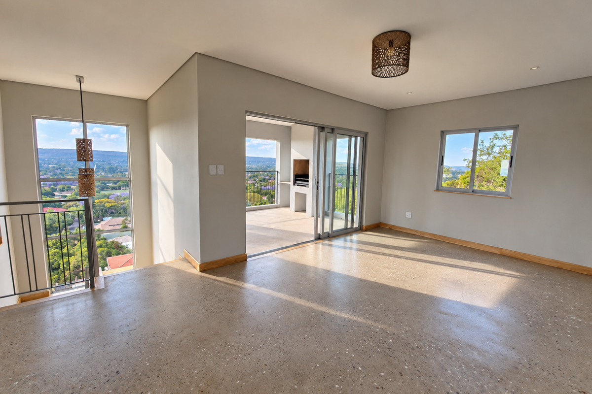 Spacious, light-filled living area featuring polished concrete floors, large windows with scenic views, and seamless access to a covered patio with a built-in braai.