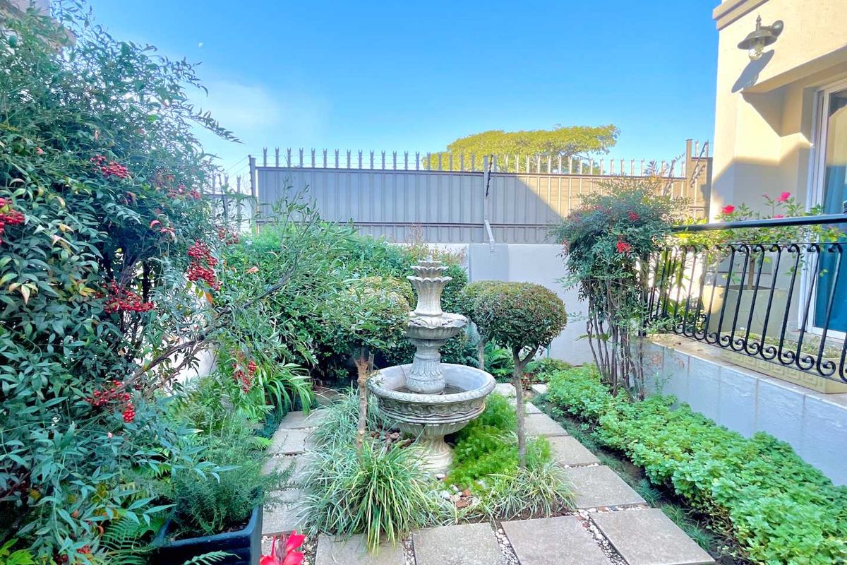A well-maintained rear garden area featuring a central stone fountain, paved pathways, and established perimeter landscaping with metal fencing.