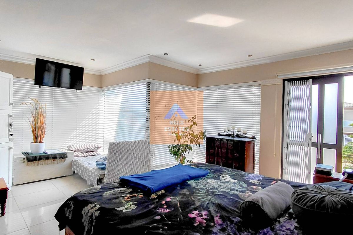 Spacious bedroom featuring tiled flooring, recessed downlights, and large windows with venetian blinds, providing access to an outdoor area through a security gate.