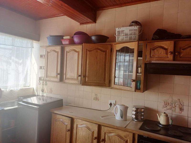 A dated kitchen featuring wooden cabinetry, tiled backsplash, and a timber ceiling, offering a functional layout with built-in cooking appliances.