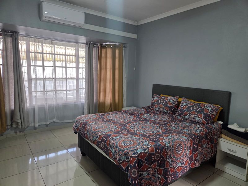 A well-maintained bedroom featuring tiled flooring, a split-system air conditioner, and a window fitted with security bars.