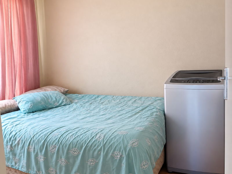 A bedroom featuring laminate flooring and neutral wall finishes, currently utilized with a bed and a portable washing machine.