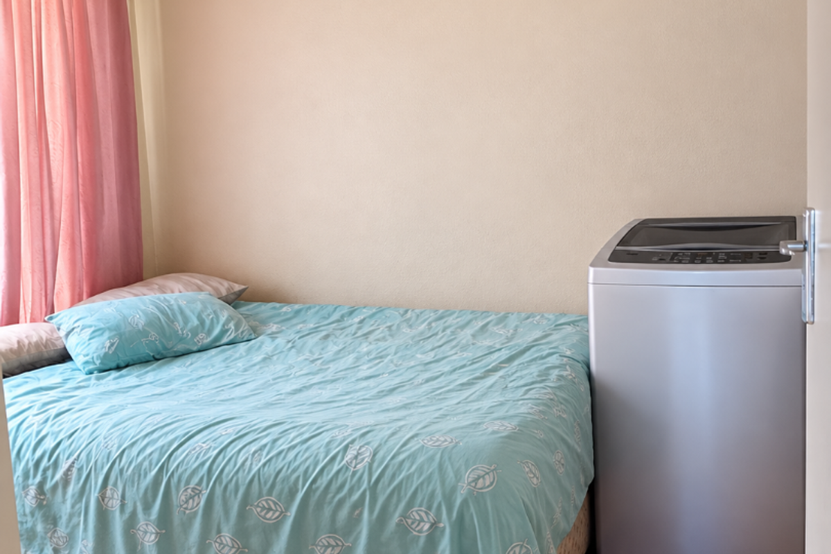A bedroom featuring laminate flooring and neutral wall finishes, currently utilized with a bed and a portable washing machine.