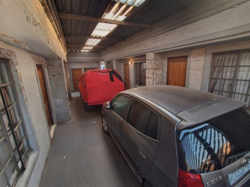 A covered garage or utility area featuring stone masonry pillars, corrugated roofing with translucent panels, and multiple access doors.