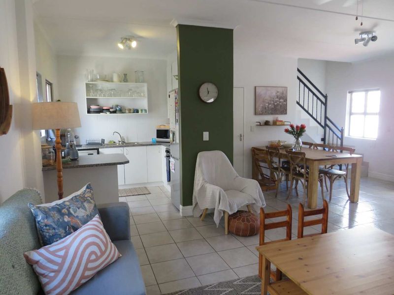 Open-plan living area featuring a functional kitchen with cabinetry, tiled flooring throughout, and a staircase leading to the upper level.