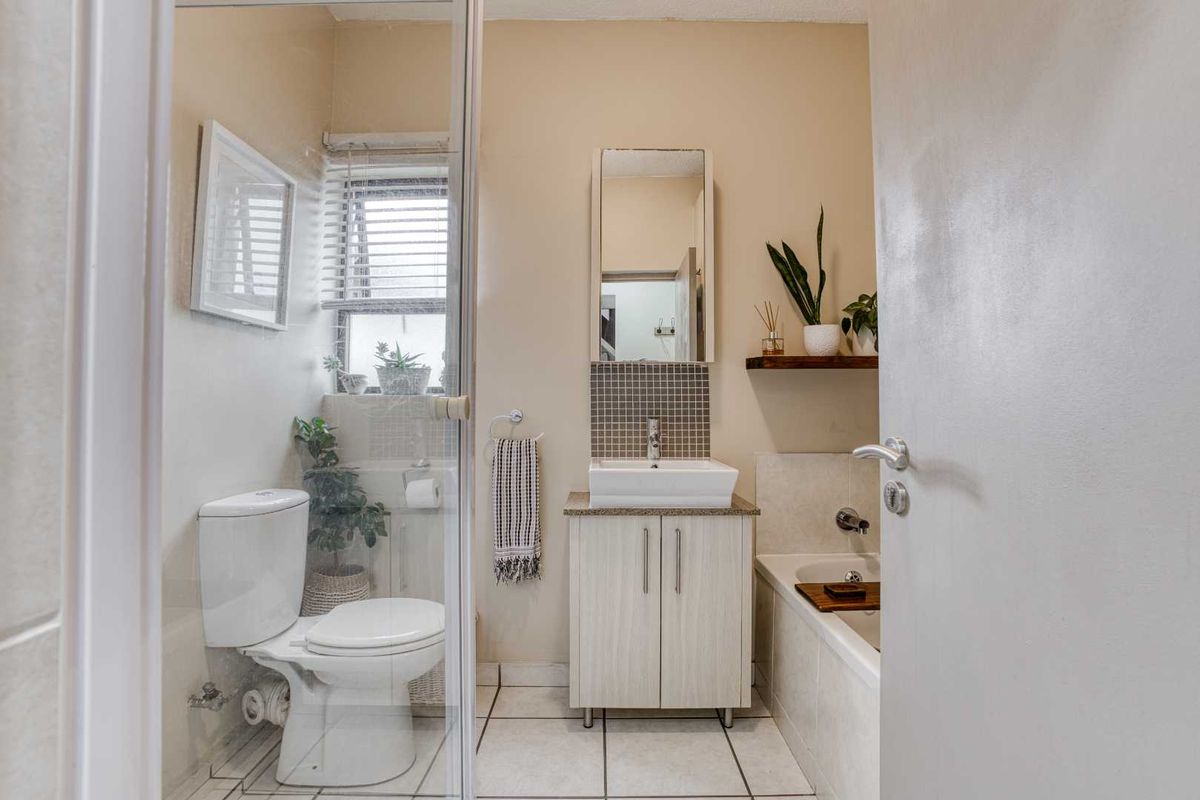 A compact bathroom featuring a vanity with a vessel sink, a built-in bathtub, and a separate glass-enclosed toilet area.