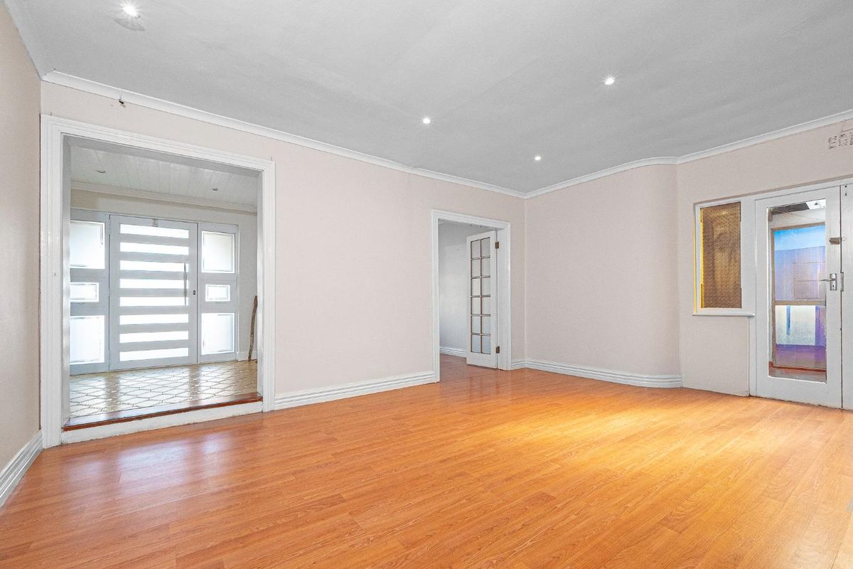 A spacious, empty living room featuring laminate flooring, recessed downlighting, and classic coved cornicing, providing a neutral canvas for interior design.