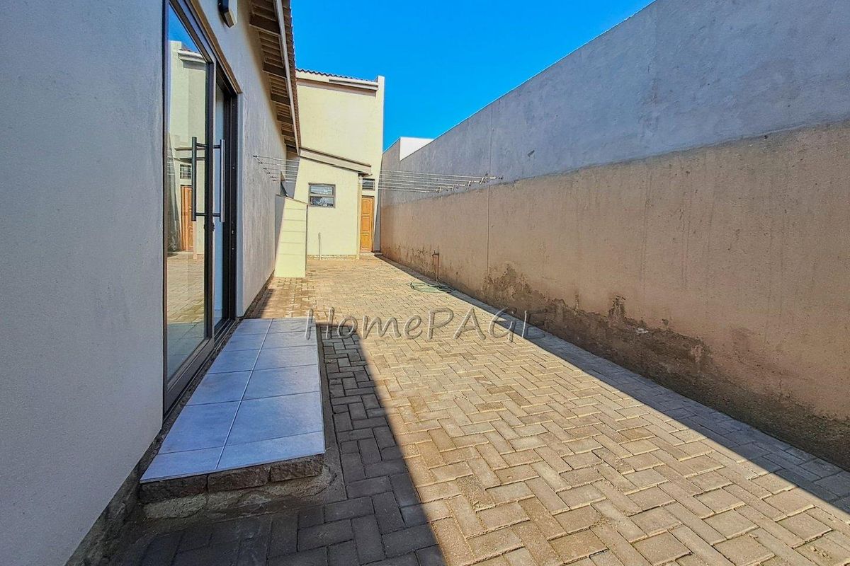 A paved side courtyard area featuring a sliding door entrance, perimeter boundary wall, and wall-mounted washing line.