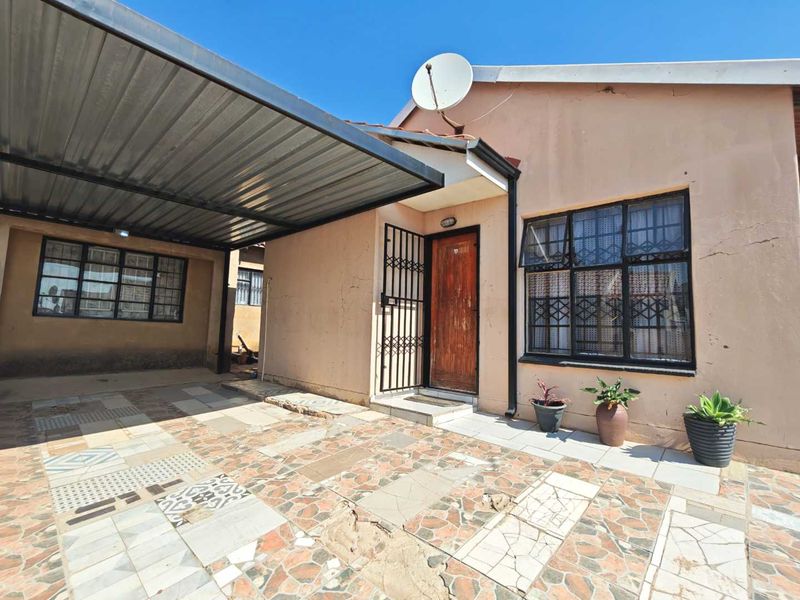 Front exterior view of the house featuring a covered carport, tiled driveway, and security features including bars on windows and a security gate.