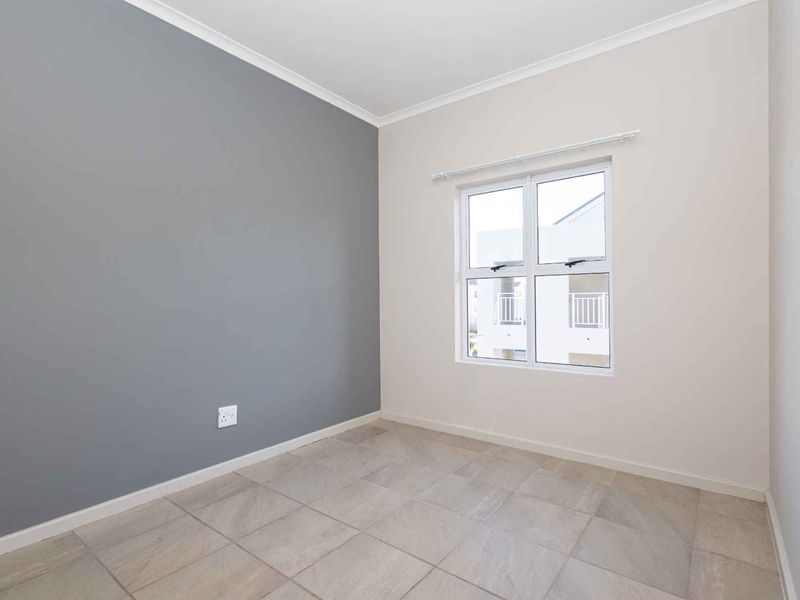 A bright, empty bedroom featuring neutral walls, a grey accent wall, tiled flooring, and an aluminium-framed window.