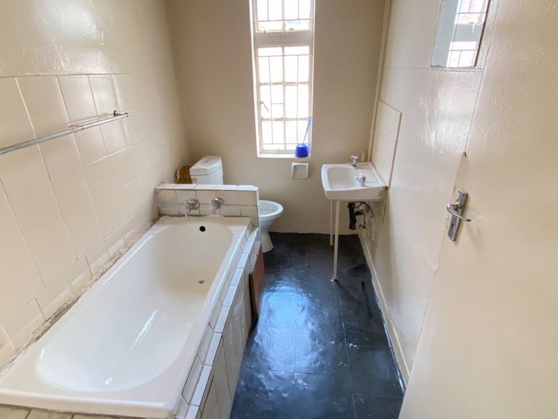 A dated bathroom featuring a built-in bathtub, pedestal sink, and toilet. The space requires renovation to update the finishes and fixtures.
