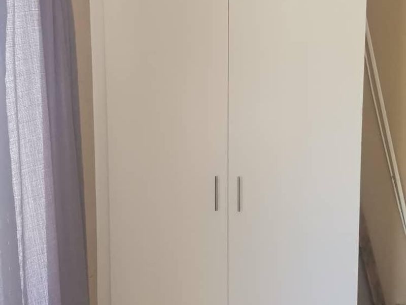 A bedroom featuring a clean, white built-in wardrobe with modern handles, providing efficient storage space.
