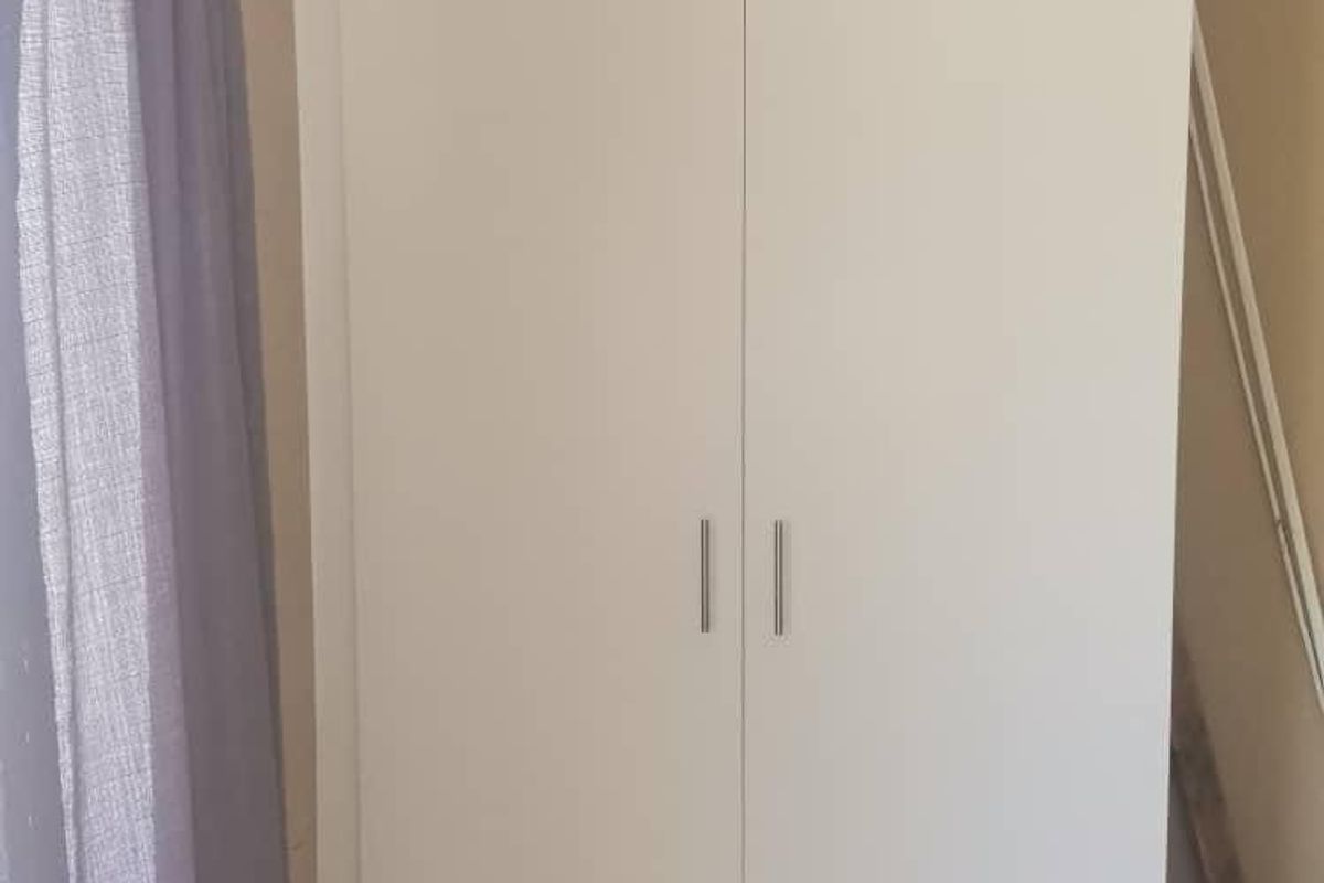 A bedroom featuring a clean, white built-in wardrobe with modern handles, providing efficient storage space.
