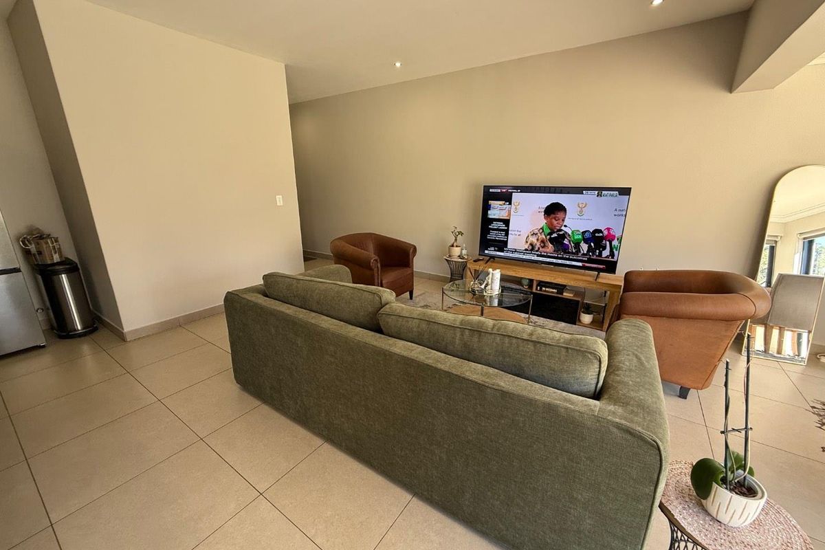 A spacious living room featuring neutral tiled flooring and recessed ceiling lighting, providing a comfortable and well-lit area for relaxation.