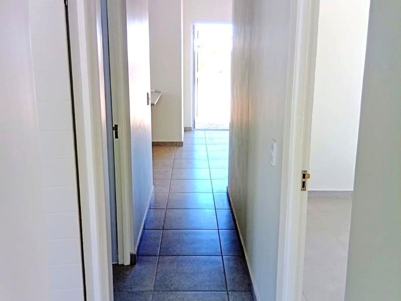 A bright, empty hallway featuring tiled flooring and a tongue and groove ceiling, providing access to multiple rooms within the home.