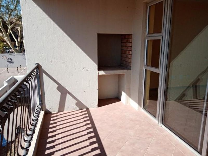 A private balcony featuring a built-in brick braai, tiled flooring, and a wrought iron balustrade, accessible via a sliding glass door.