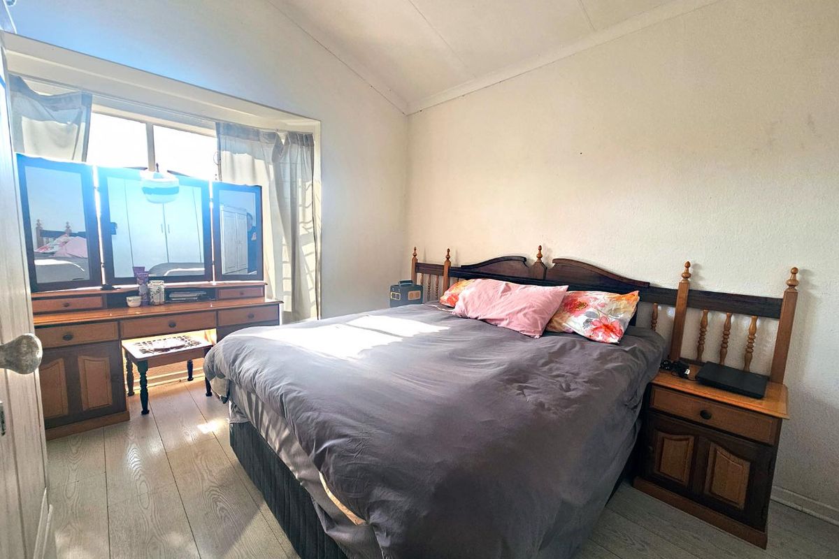 A bedroom featuring laminate flooring and a large window allowing natural light, providing a functional space for rest.