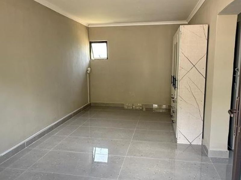 A clean, empty bedroom featuring neutral wall tones, modern grey tiled flooring, and a built-in wardrobe with a marble-effect finish.