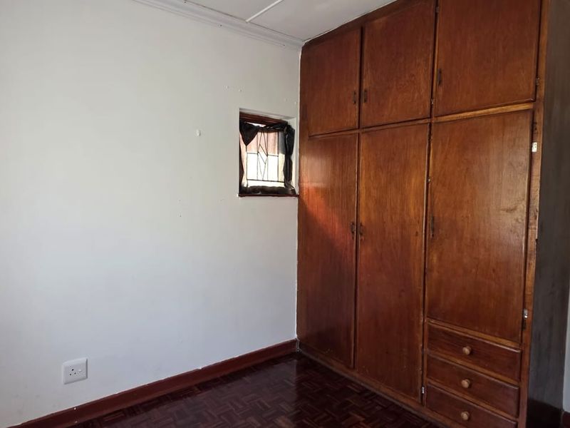 A bedroom featuring classic parquet flooring and built-in wooden cupboards, offering a functional space ready for modern updates.