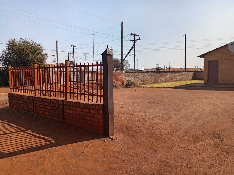 A spacious rear yard area featuring a brick boundary wall, metal palisade fencing, and an outbuilding on an unpaved plot.