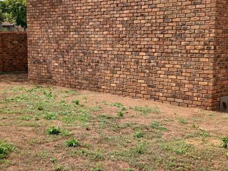 A view of the rear exterior brick wall and gable roofline of the house, set against an unlandscaped yard.