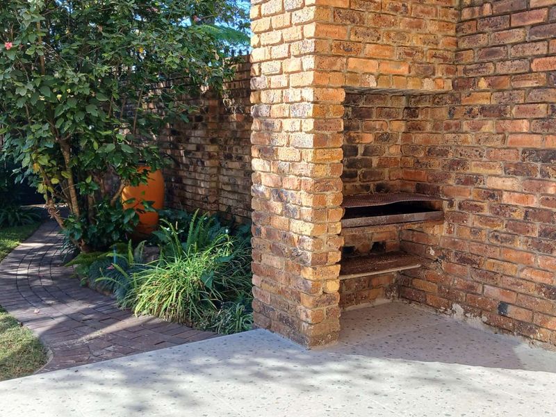 Outdoor patio area featuring a built-in brick braai, paved garden path, and established landscaping, providing a functional space for outdoor entertaining.