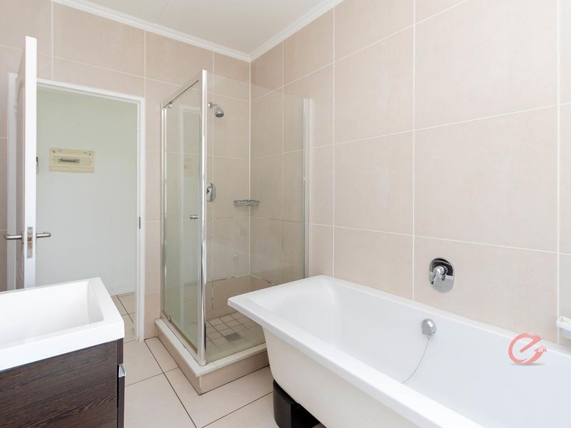 A clean, modern bathroom featuring a glass shower enclosure, a freestanding bathtub, and a vanity unit with neutral wall and floor tiling.