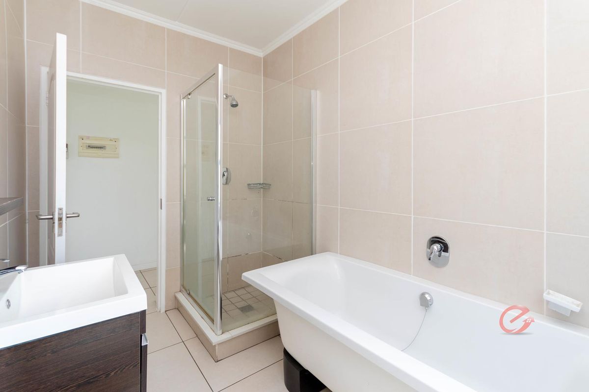 A clean, modern bathroom featuring a glass shower enclosure, a freestanding bathtub, and a vanity unit with neutral wall and floor tiling.