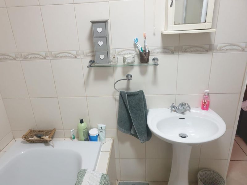 A functional bathroom featuring a pedestal sink, built-in bathtub, and neutral wall tiling with a wall-mounted medicine cabinet.