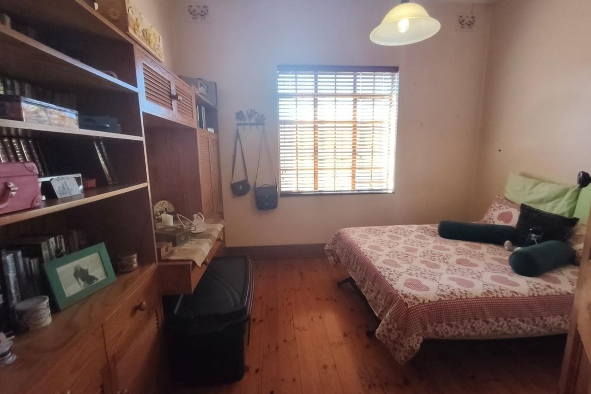 A bedroom featuring polished timber flooring, a window with venetian blinds, and a central pendant light fixture.