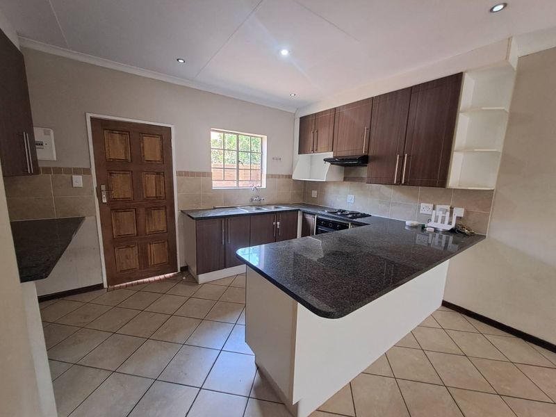 A functional kitchen featuring dark wood cabinetry, granite countertops, a built-in hob with extractor fan, and neutral tiled flooring throughout.